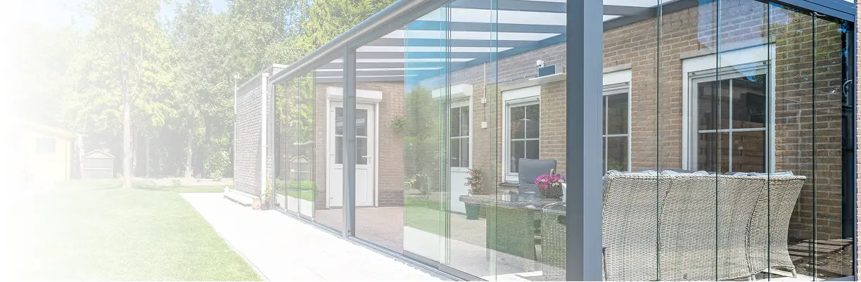 Terrassenüberdachung Glas mit Alu-Rahmen und Schiebetüren vor einem Wohnhaus mit Sitzgruppe auf Terrasse